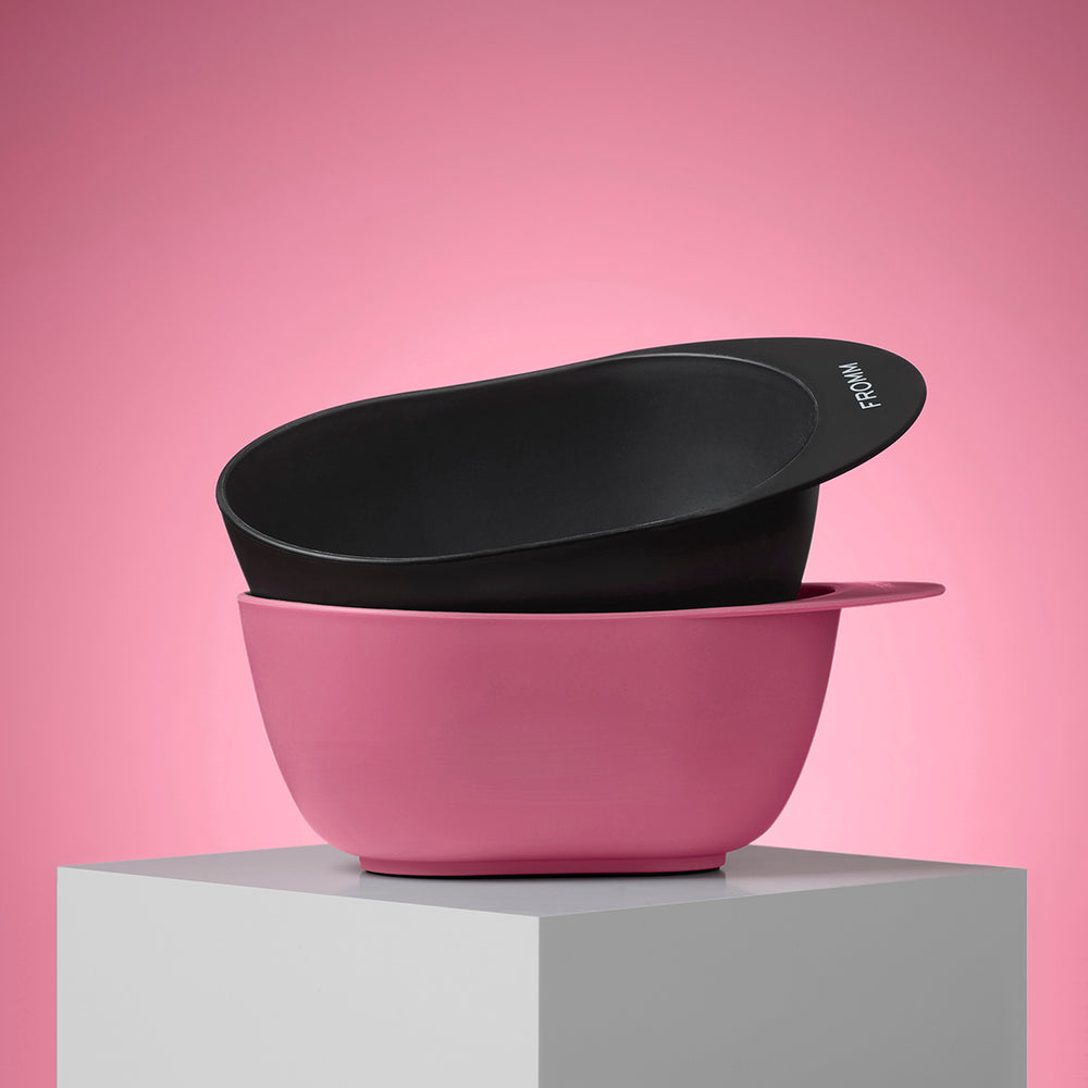 Two color mixing bowls, one black and one pink, stacked on a gray platform with a pink background.