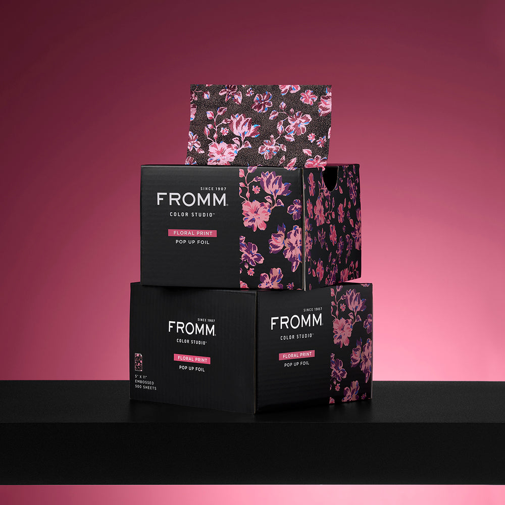 Stack of FROMM Color Studio floral foil boxes on a pink and black background