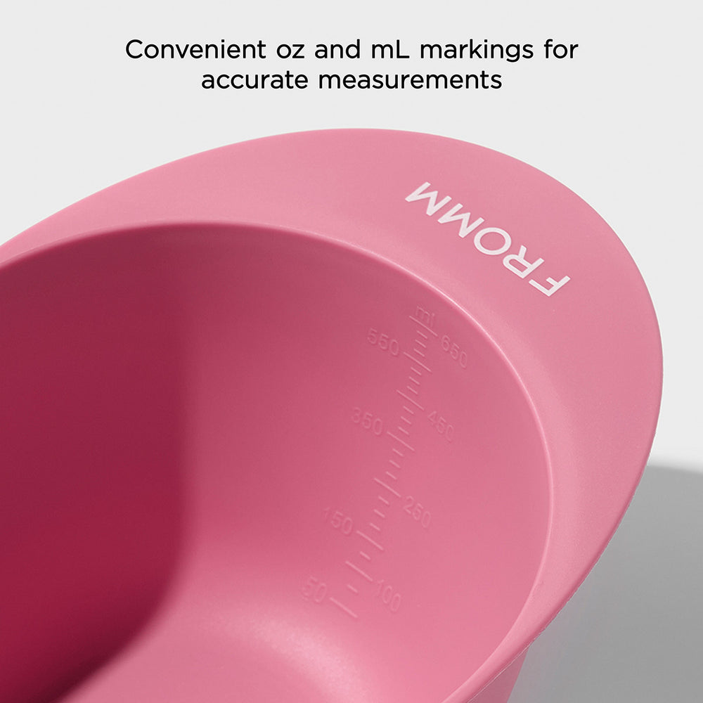 Pink measuring hair color bowl with oz and mL markings on a light gray background