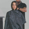 Barber putting on model a navy blue camo barber cape 